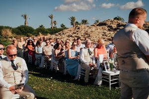 Outdoor wedding ceremony setup with white chairs arranged on a grassy lawn under blue skies with puffy clouds.