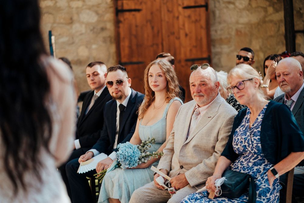 Wedding guests react with joy and emotion during a ceremony in a rustic stone venue.