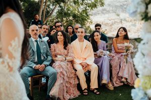 Wedding guests seated outdoors at a garden ceremony with soft pink and purple attire creating a romantic atmosphere.