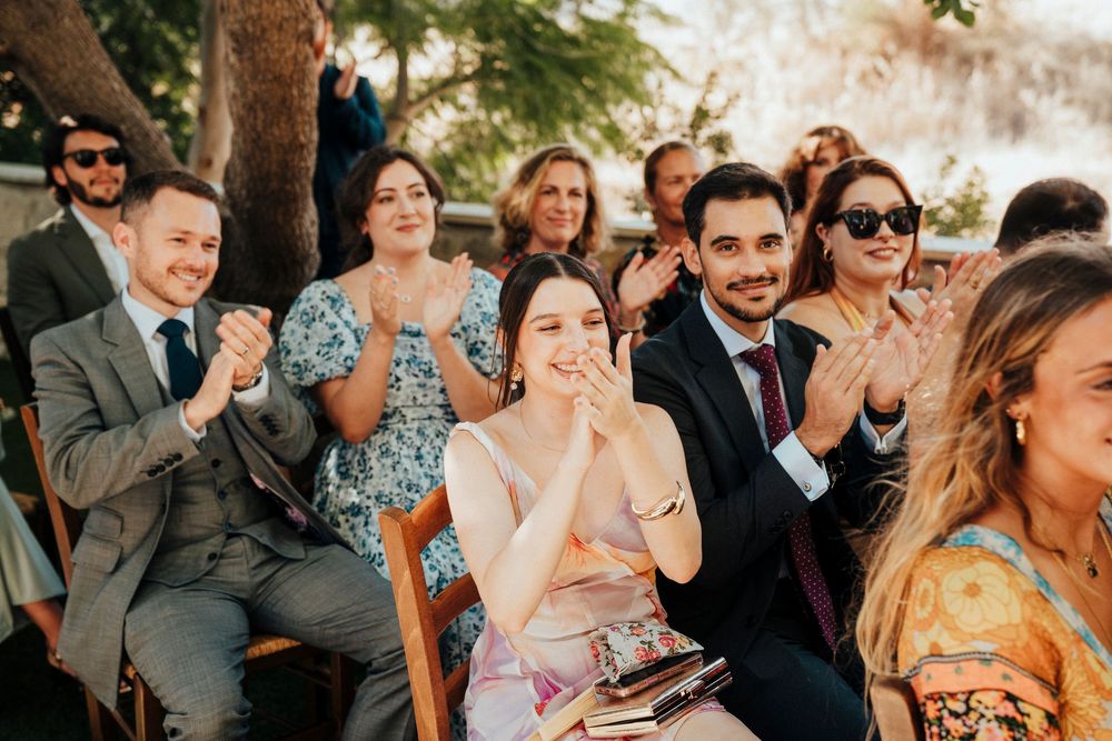 Wedding guests react emotionally during an outdoor ceremony as golden sunlight filters through the trees.