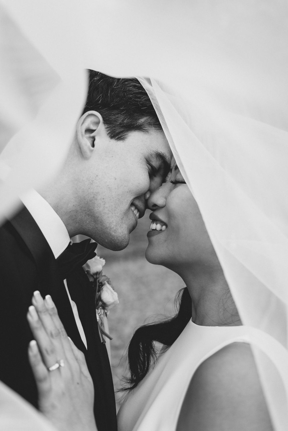 A romantic black and white wedding photo captures a tender moment between a bride and groom under a veil.
