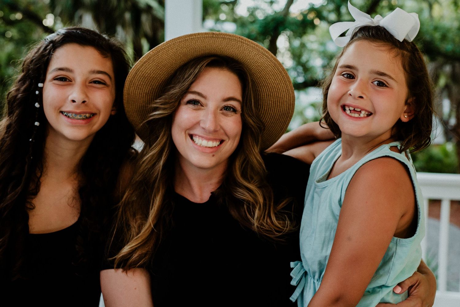 Three people pose together on a porch, with one wearing a sunhat.
family photography