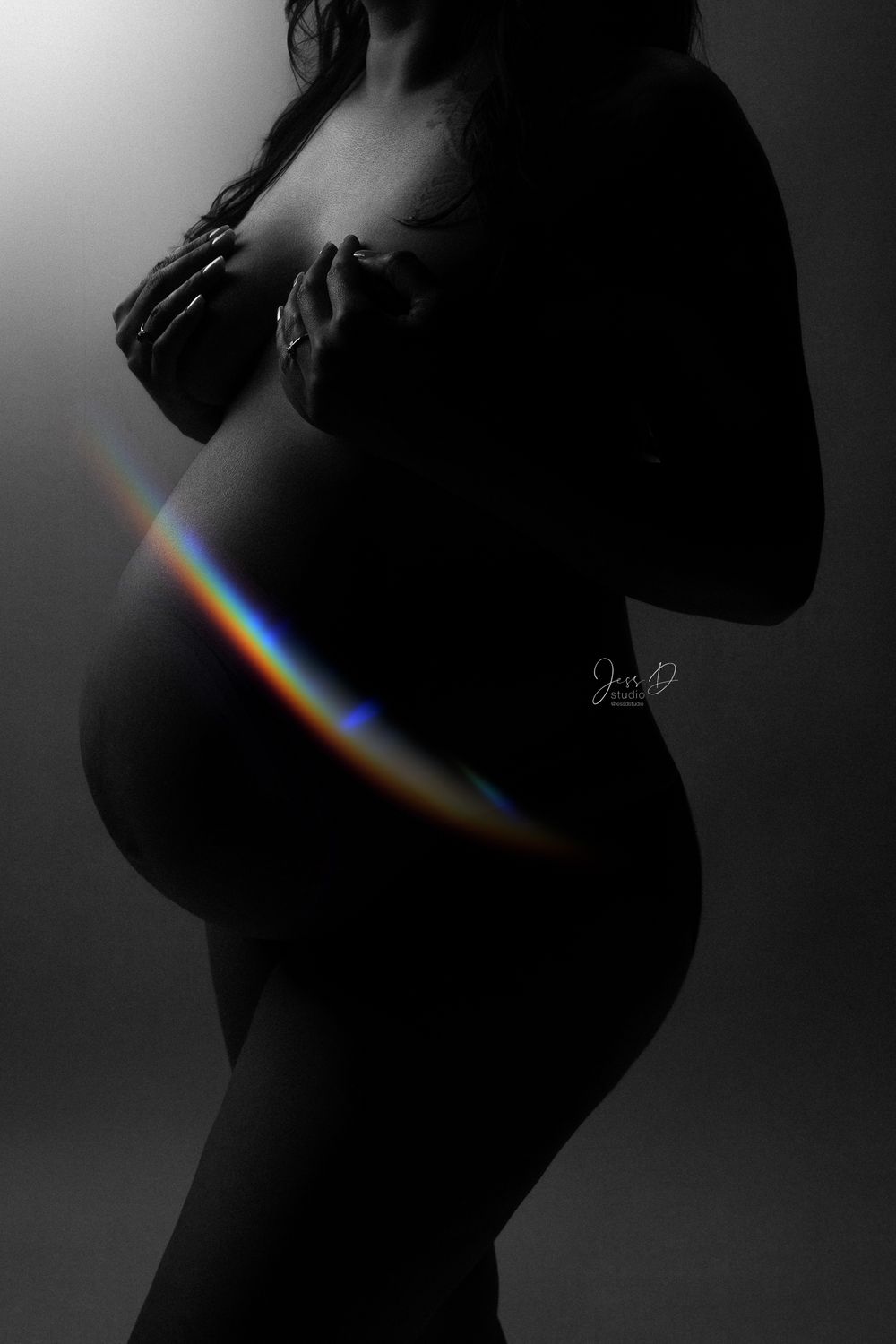 Black and white image of mother to be with rainbow across her belly in studio.