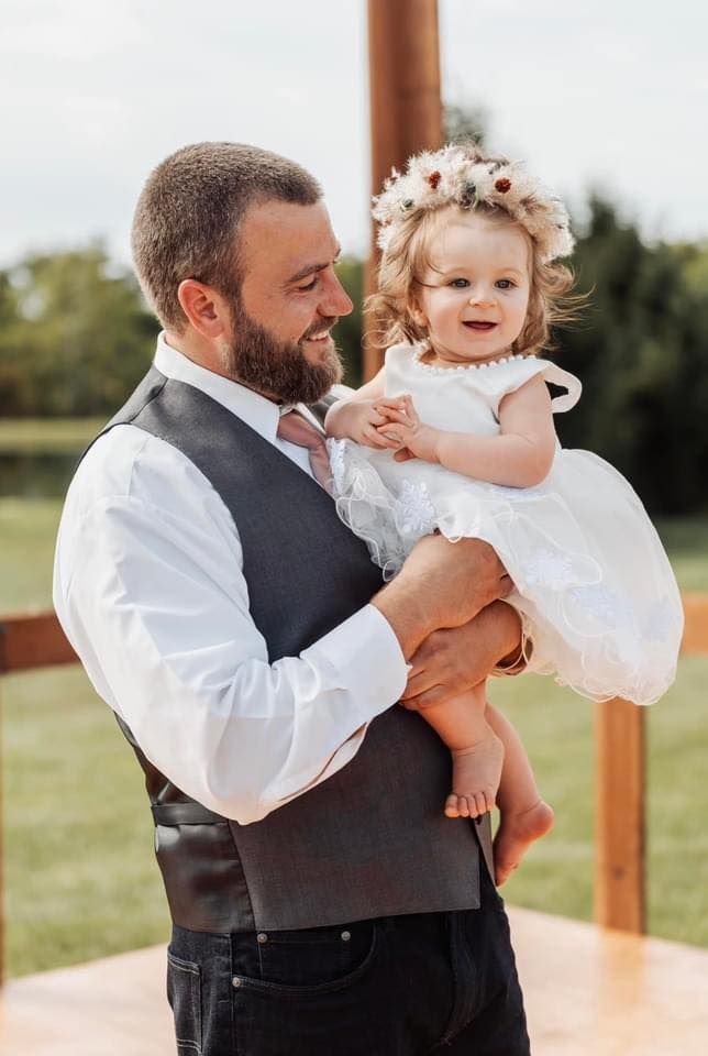 A tender moment at a wedding between two adorable figures wearing formal white attire against a sunny outdoor backdrop.