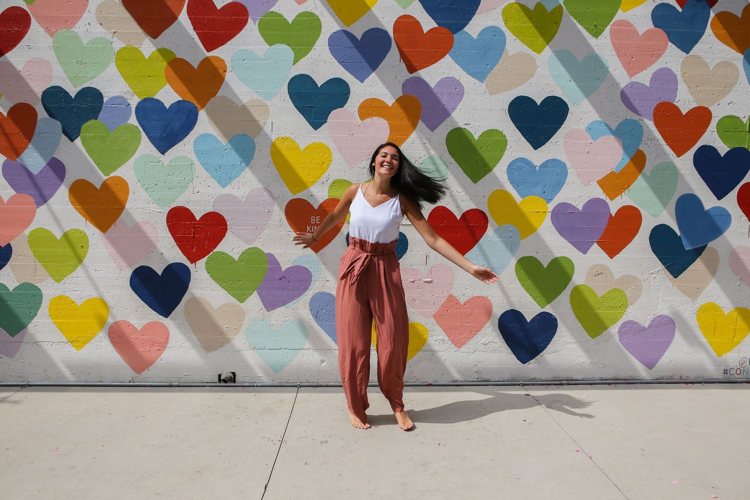 Senior high school girl dancing barefoot in front of the Confetti Heart Wall in Charlotte, NC.  Casting shadows