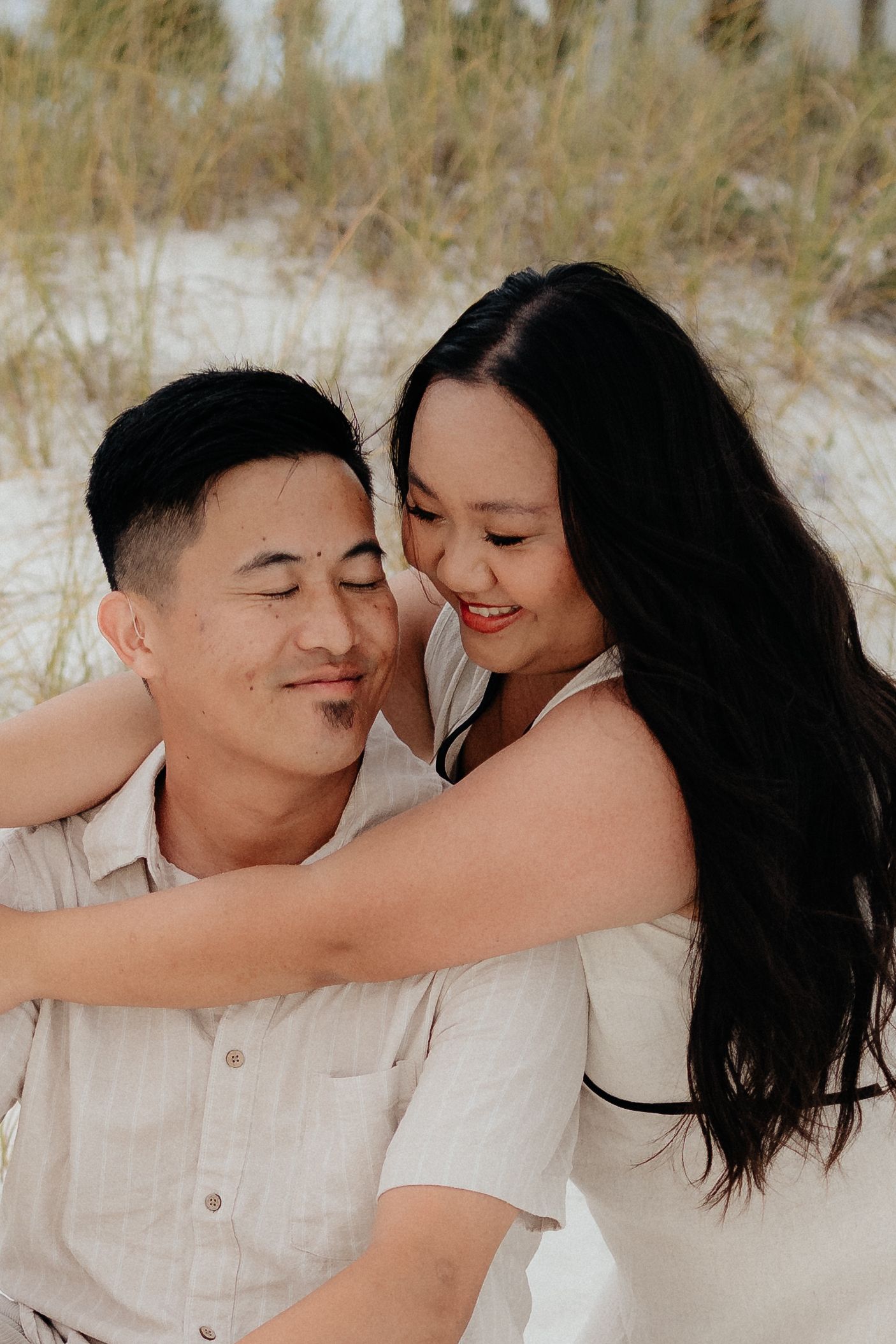 Romantic couple embracing in tall grass field during sunset.
