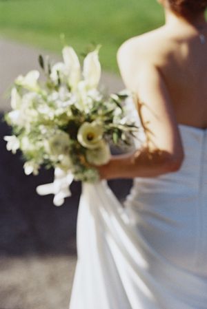 Beautiful film portrait of a white bridal bouquet with delphiniums and roses against a dreamy outdoor wedding background.