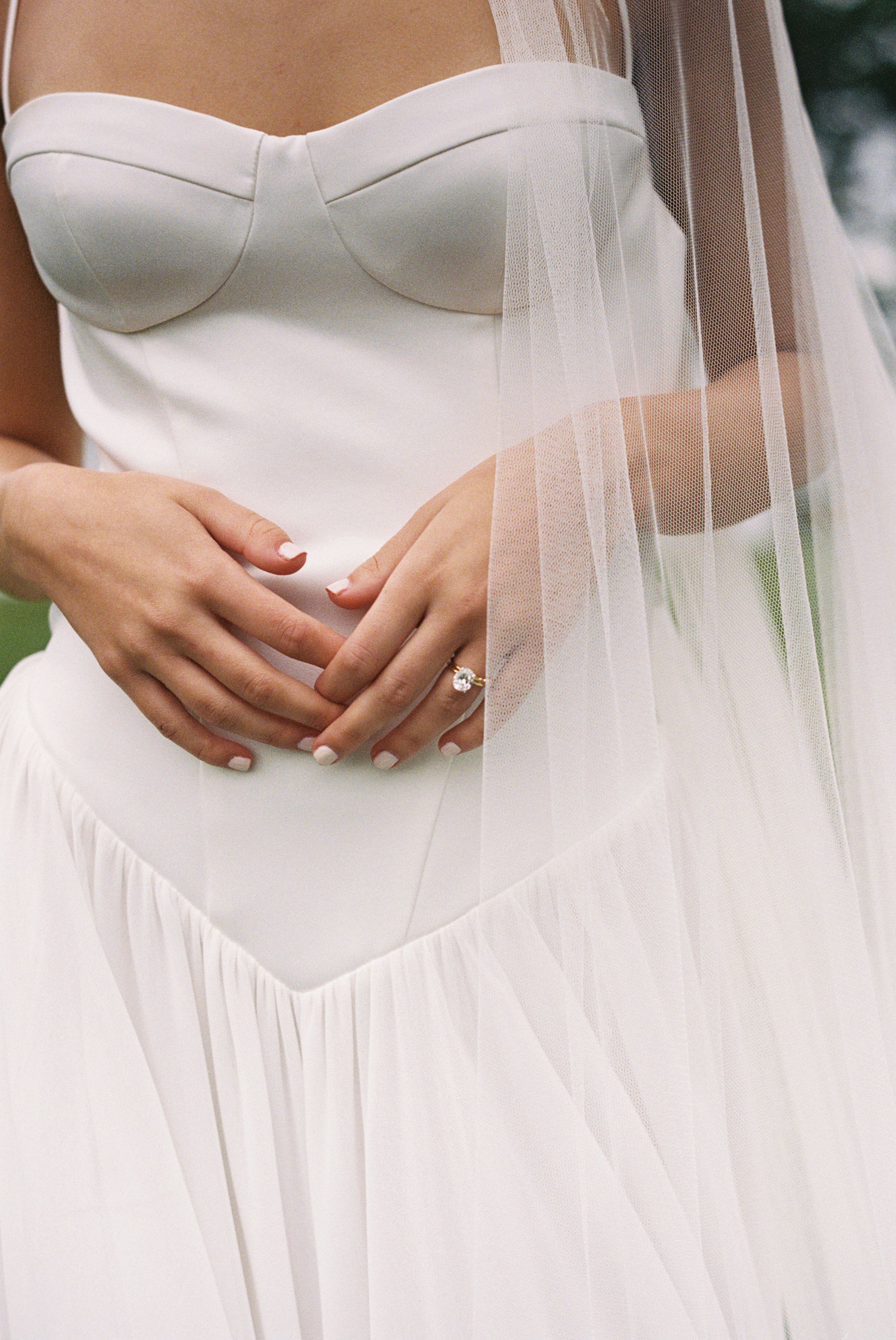 A close-up view of hands holding a bridal veil against a white wedding dress bodice.