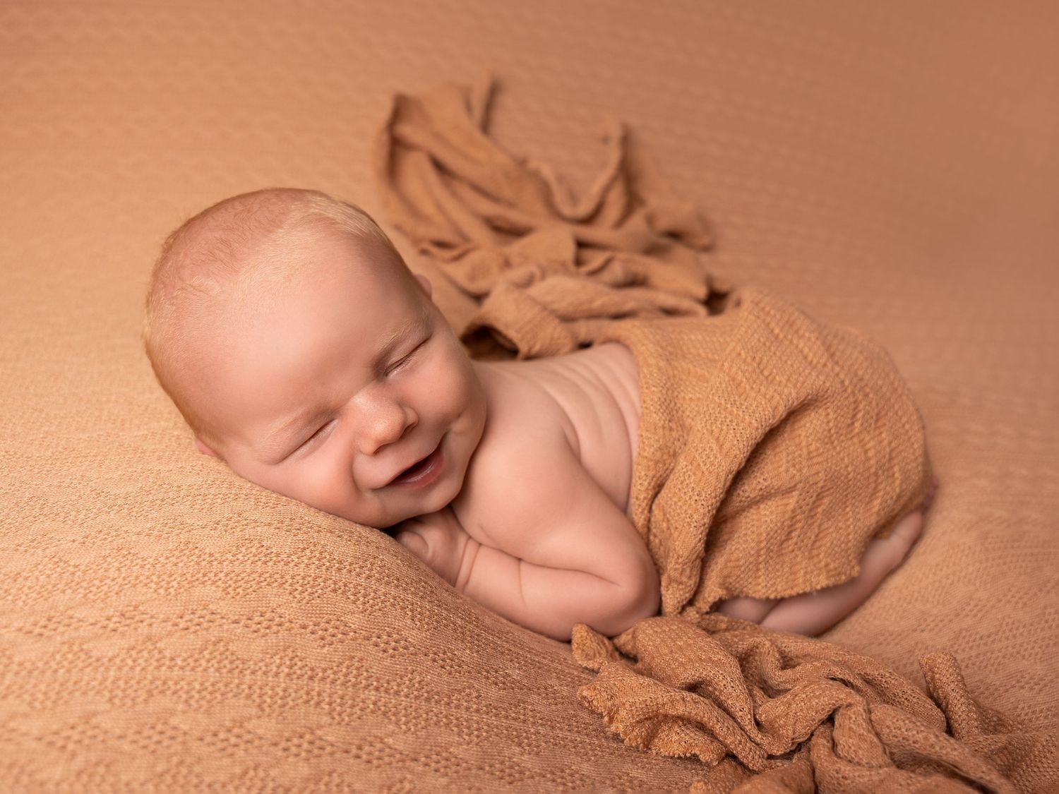 Sleeping baby boy posed on brown textured blanket, smiling at his newborn photoshoot in Doncaster