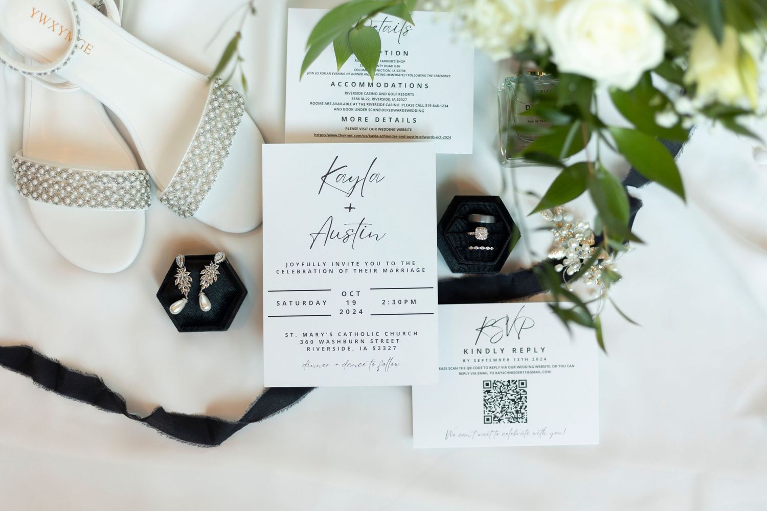 Wedding details flat lay with invitation, white shoes, and floral elements on light fabric.