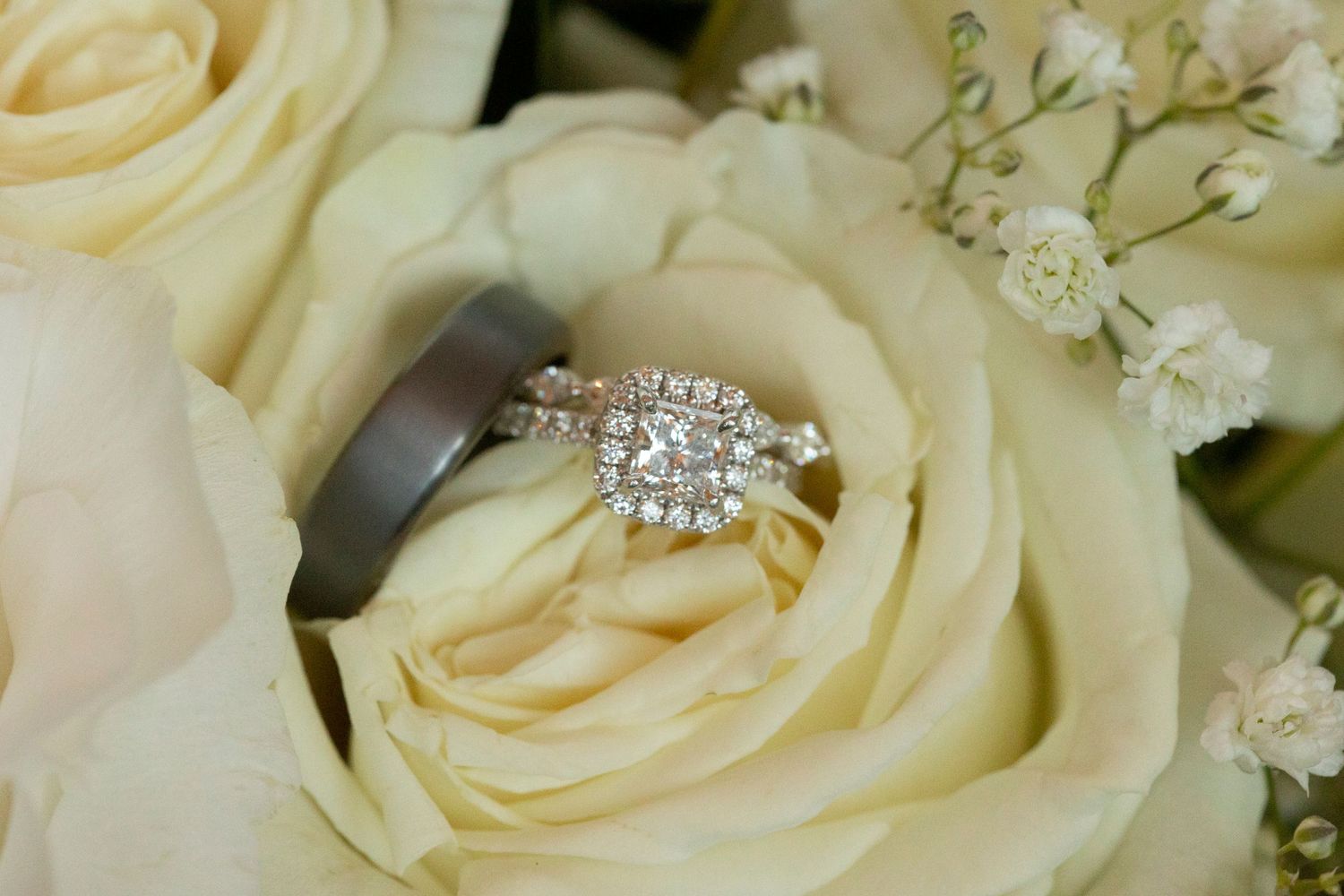 Diamond engagement ring nestled in the center of a creamy white rose with delicate baby's breath accents.