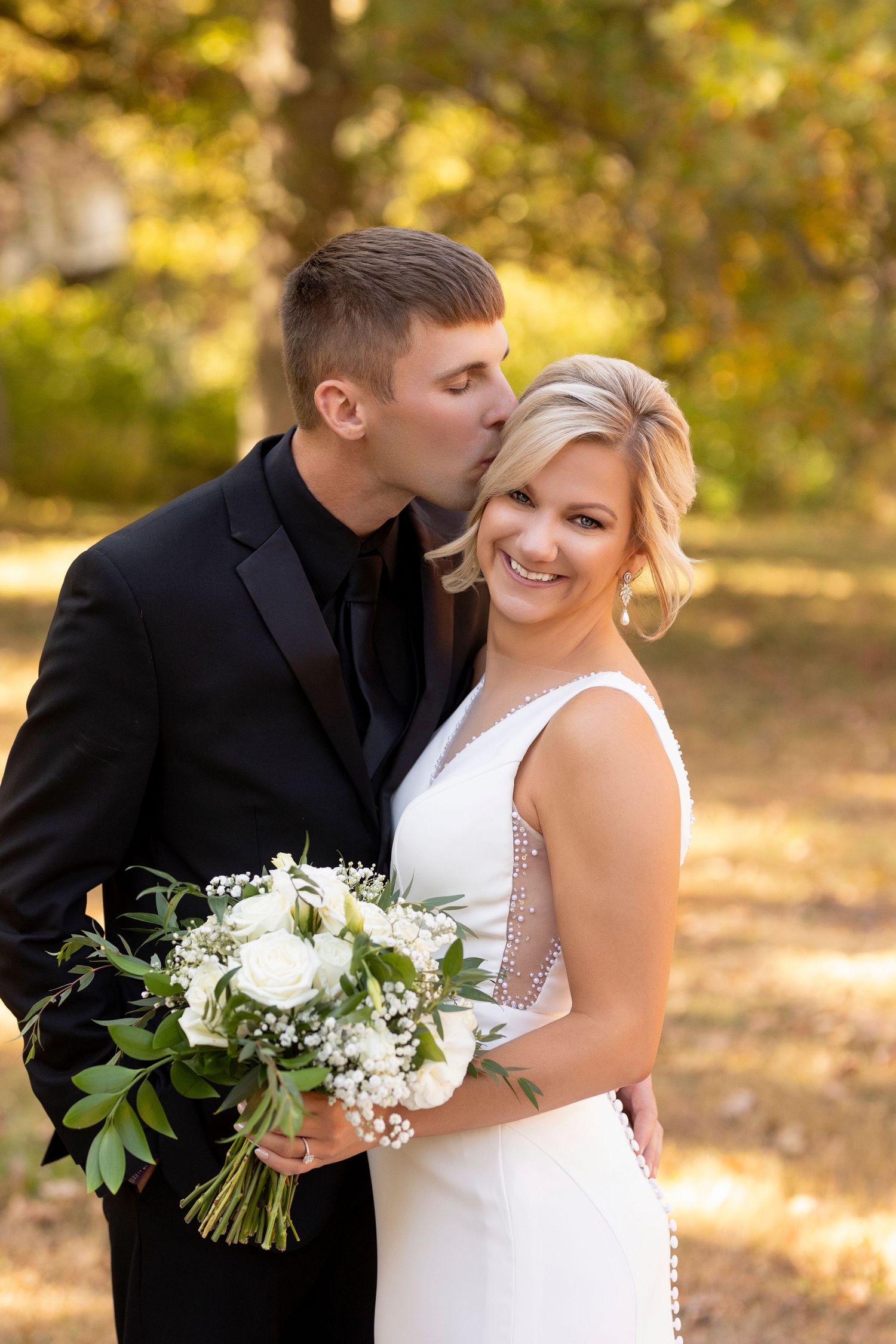 Joyful wedding moment captured in golden autumn sunlight with white floral bouquet.