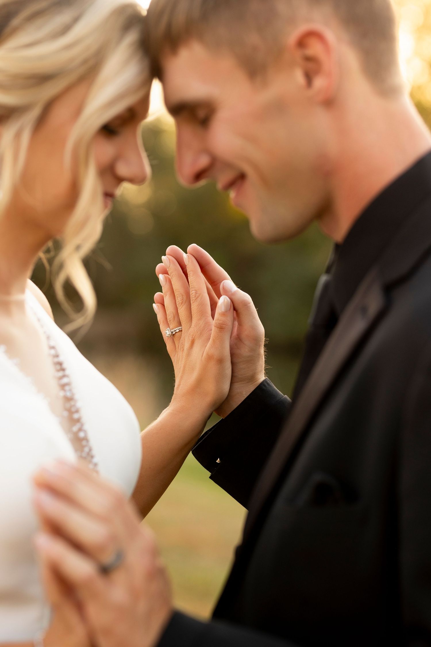 Close-up of joined hands showing engagement ring in warm sunset lighting.