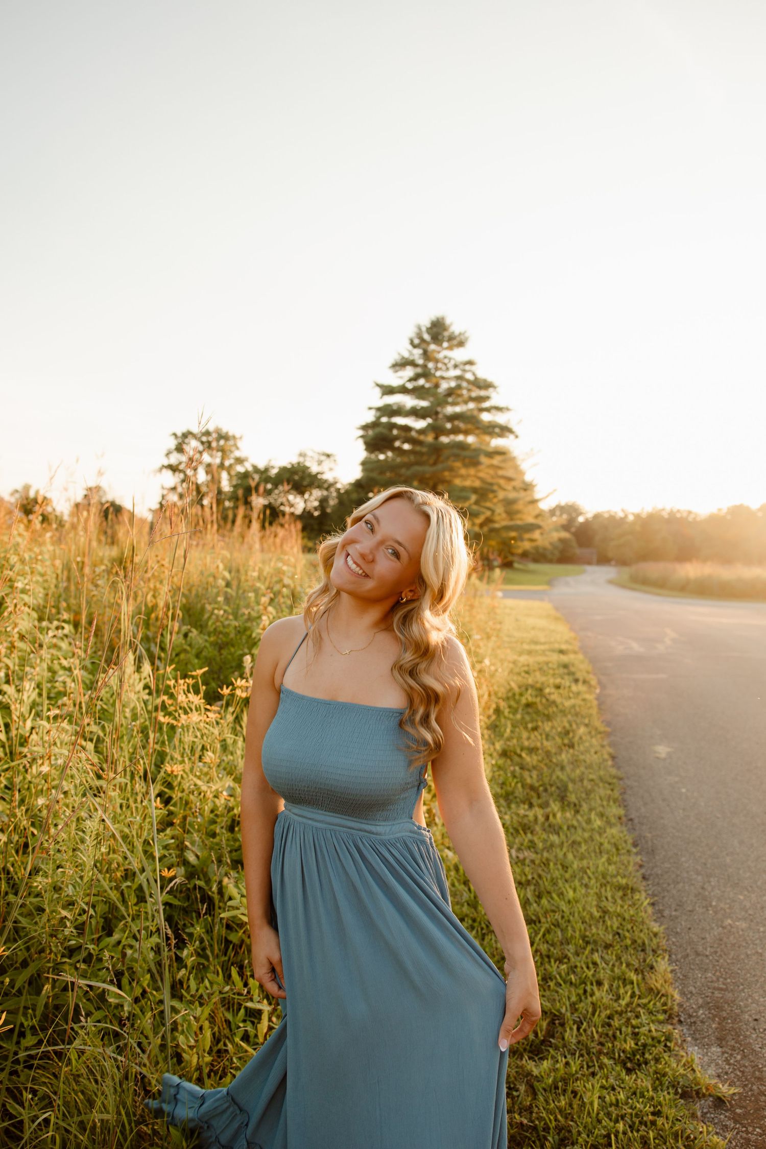 Woman in teal dress posing in a field at golden hour sunset.