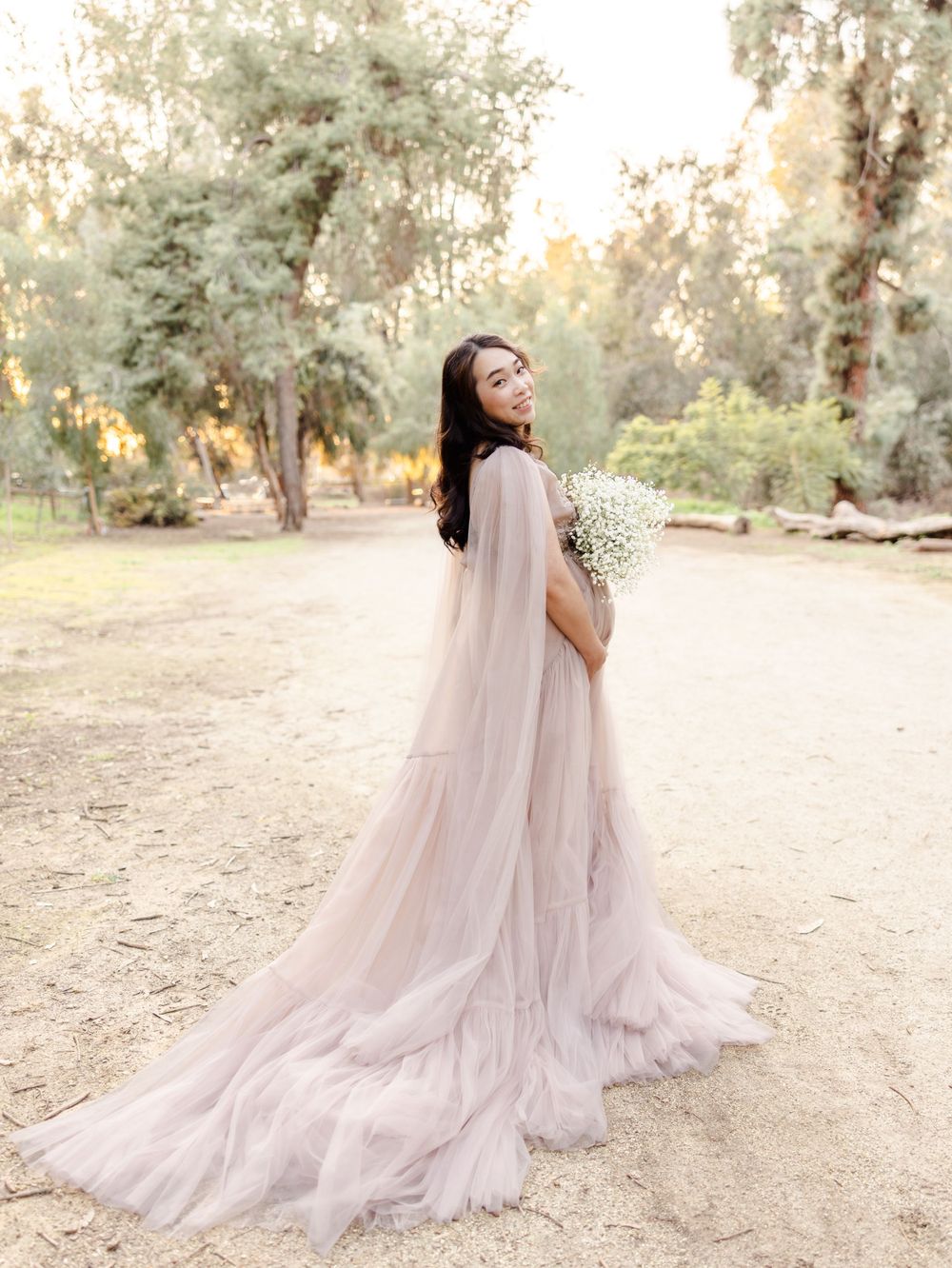 Ethereal maternity photos showcase flowing pink gown against natural outdoor backdrop.