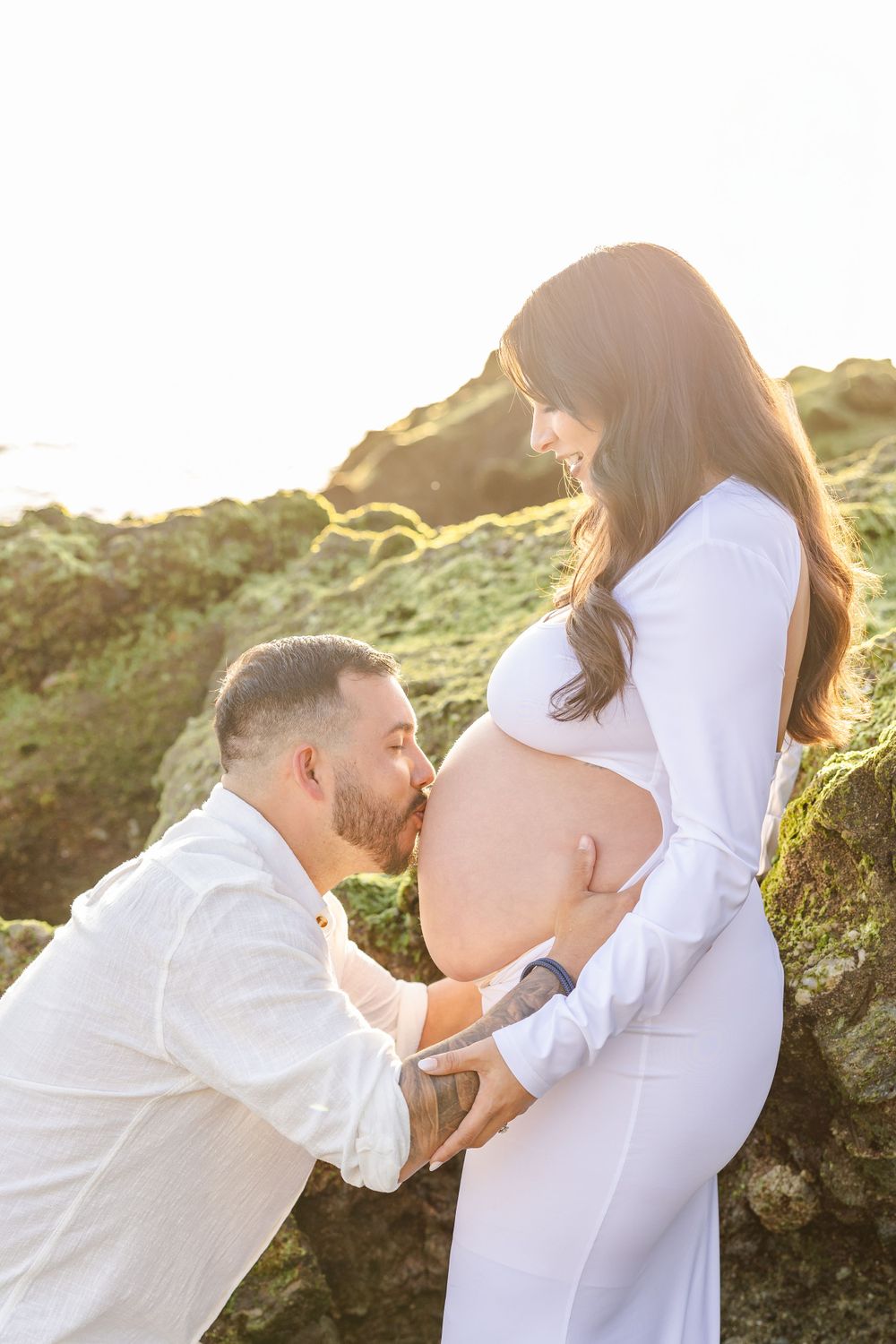 Maternity photoshoot at sunset with couple on rocky beach terrain.