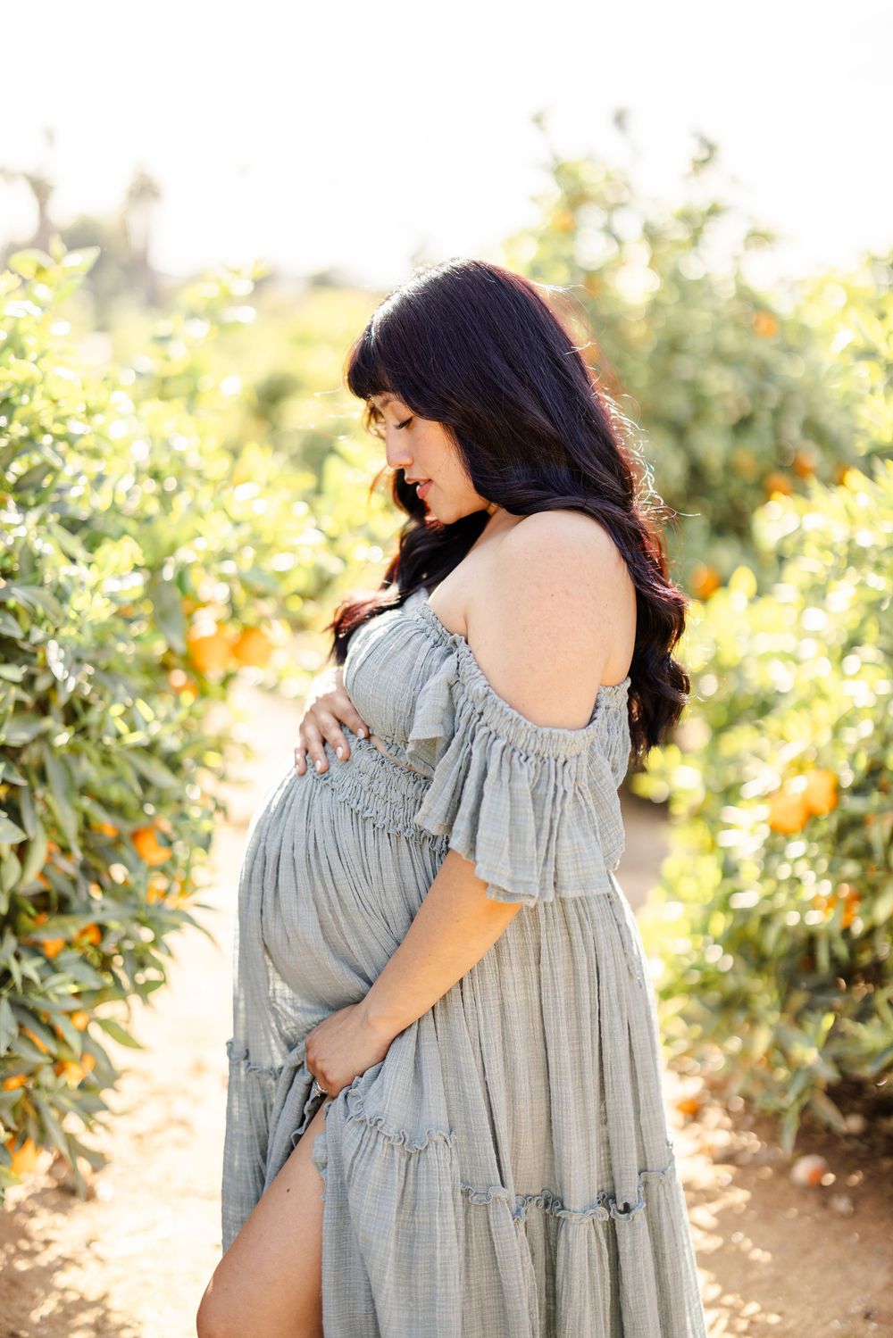 A couple embraces tenderly in an orange grove wearing coordinated grey and white outfits.
