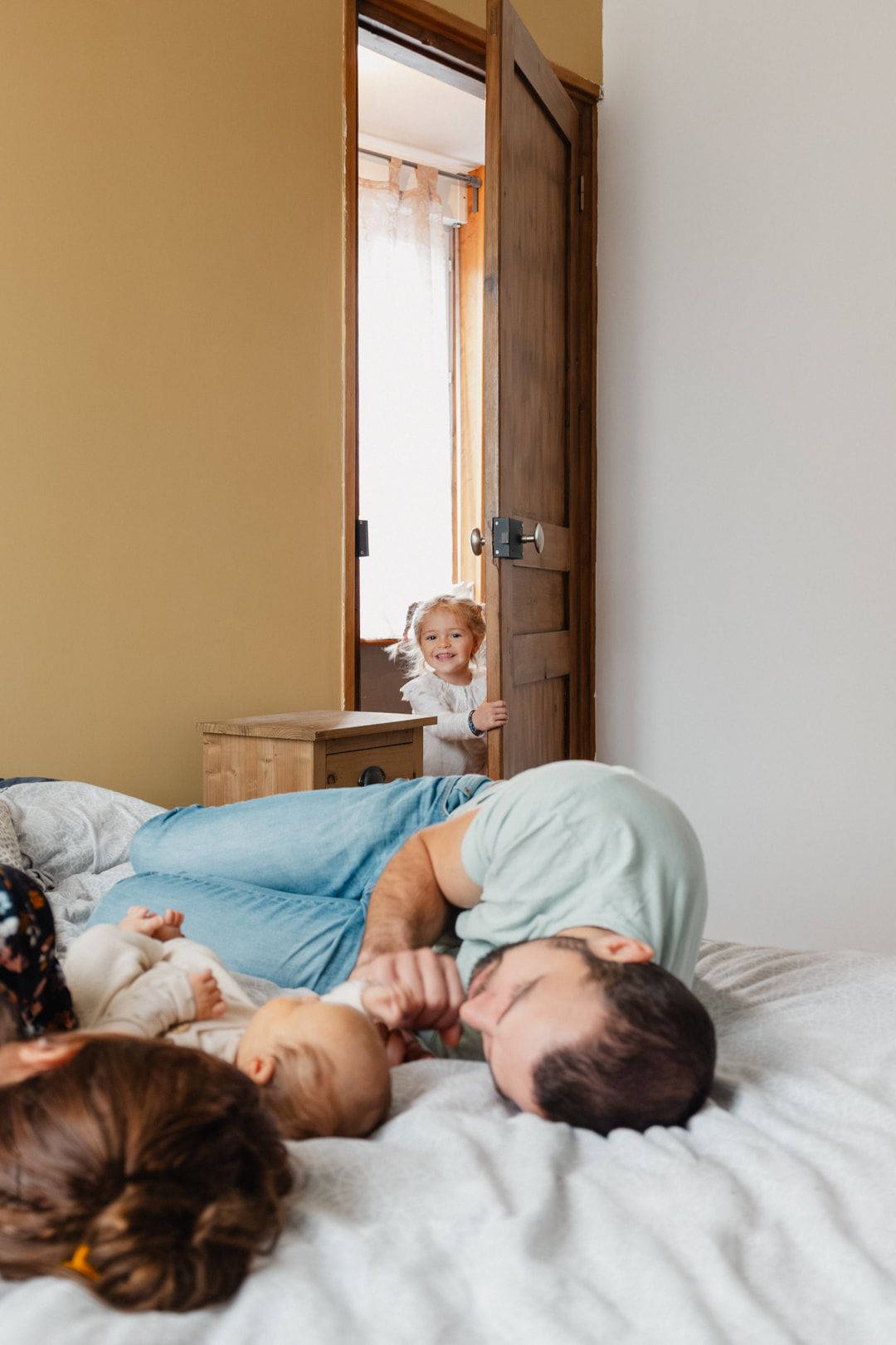 petite fille espiegle et joyeuse qui ouvre la porte de la chambre des parents en seance photo famille naissance lifestyle a Lille