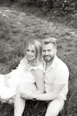 A black and white portrait of a couple sitting close together outdoors during a photoshoot.