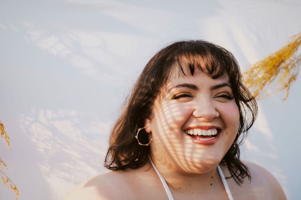 Portrait of someone against blue sky and clouds, laughing joyfully with sunlit hair blowing in the wind.