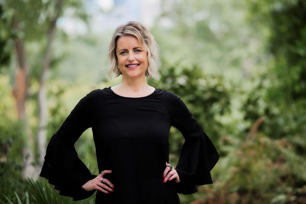 A person in a black bell sleeve top poses confidently against a blurred natural green background.