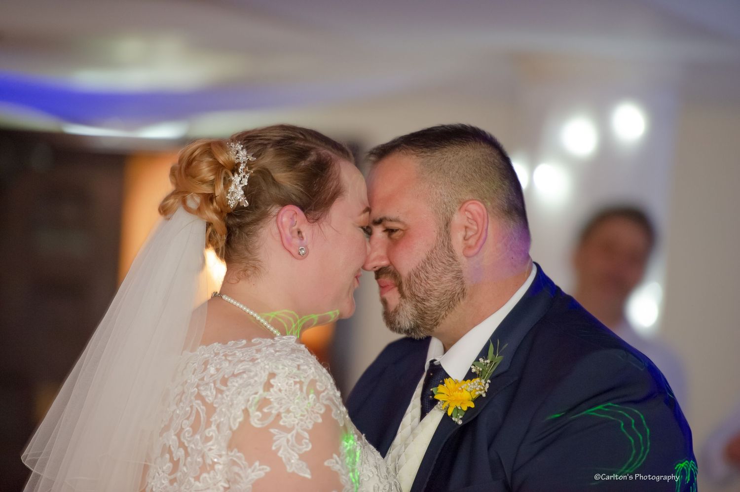 Tender moment between newlyweds touching foreheads during wedding reception.