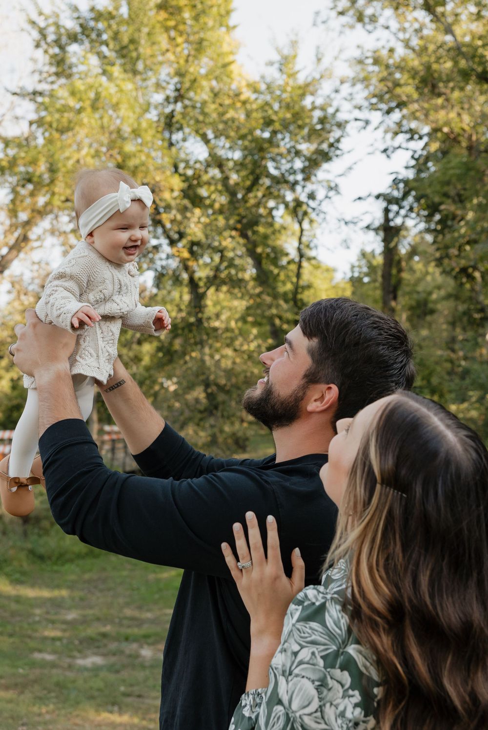 A joyful family moment outdoors as they lift their baby up in the air.