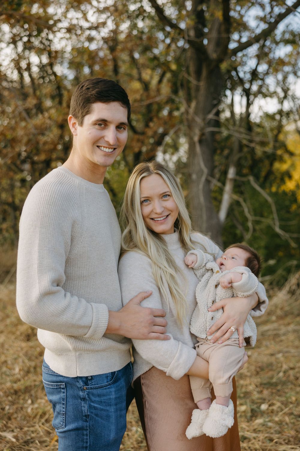Family of three poses outdoors in autumn setting with their newborn baby.