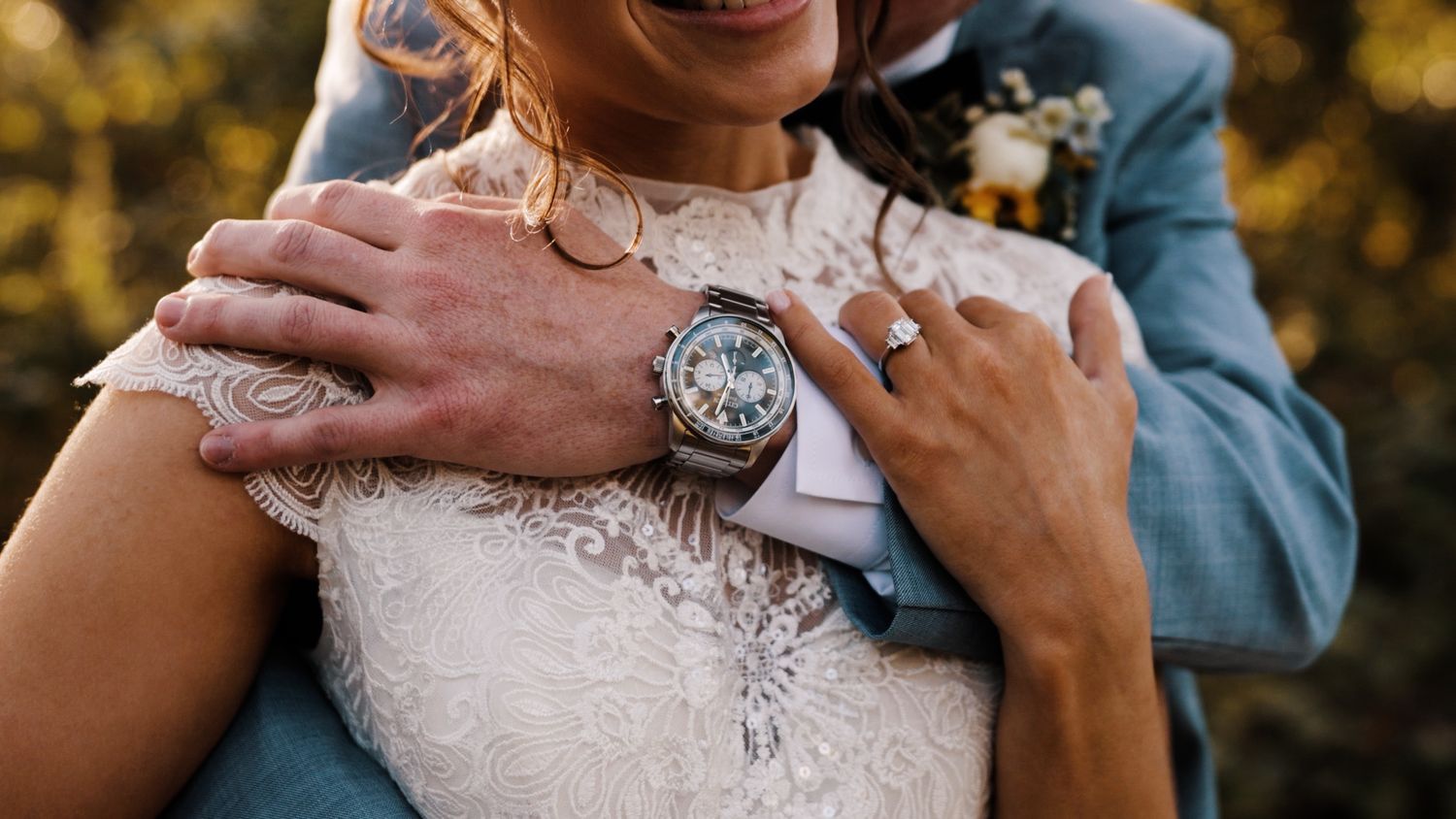 A wedding couple stands together on grass, showing the bride in a white lace dress and groom in dark suit with bouquet.
