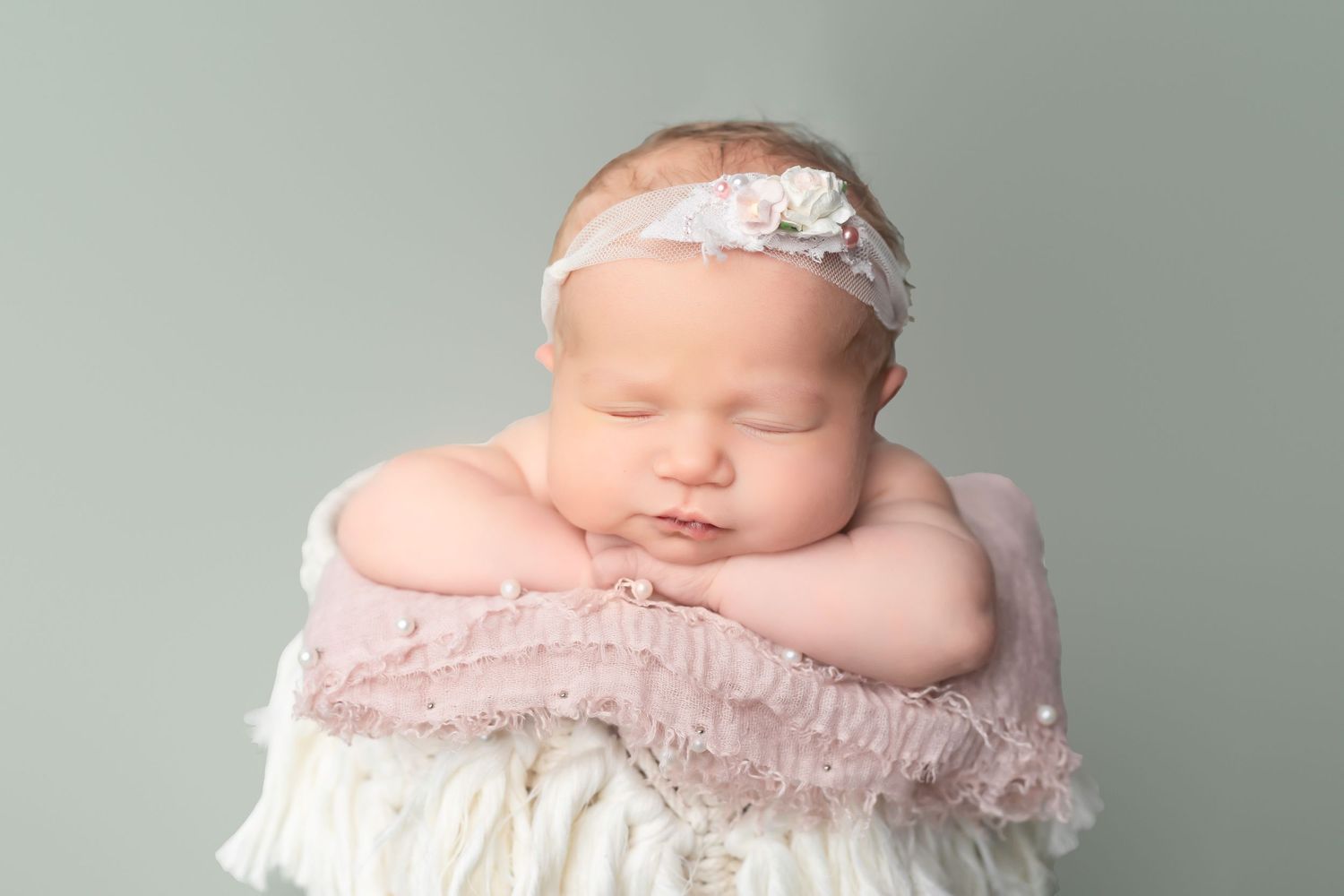 Sleeping newborn with lace headband resting on soft textured fabric in cream tones.