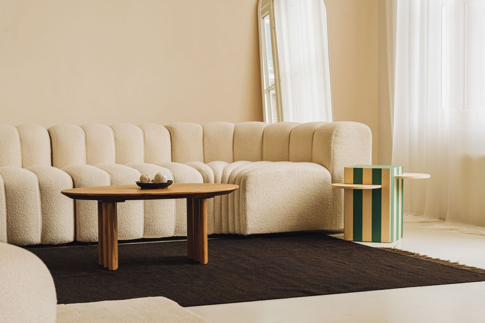 Modern living room with cream channel-tufted curved sofa, round wooden coffee table, and dark area rug.