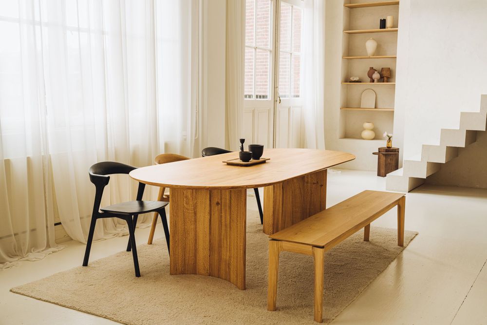 Modern dining area featuring wooden round table with black chair and wooden bench seating.