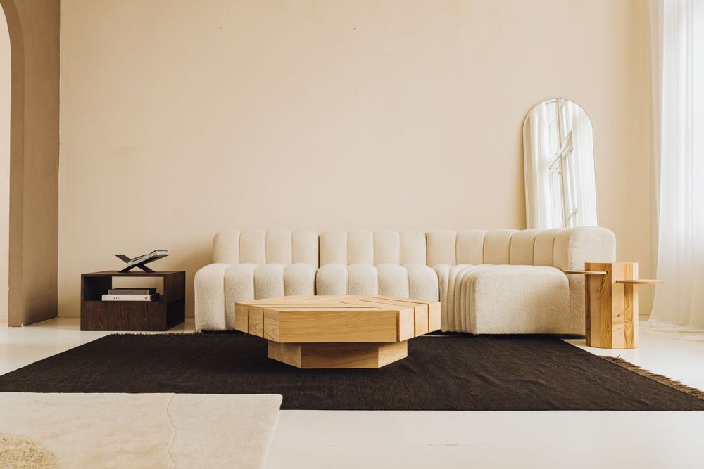 Minimalist living space with curved cream sofa, round tiered tables, and black carpet.