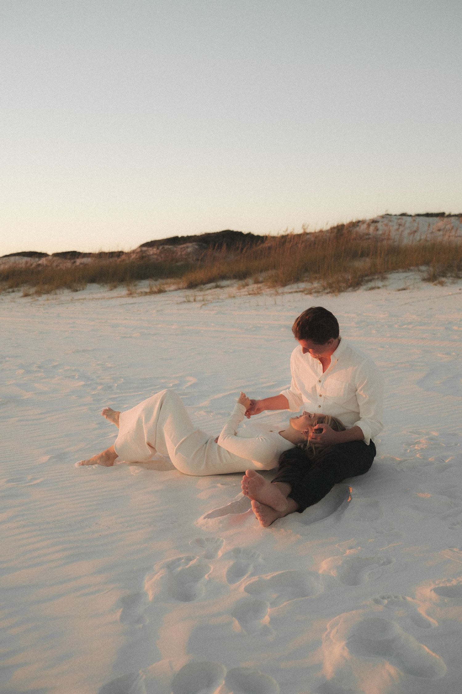 Couple playfully lying in soft white sand at the beach.
