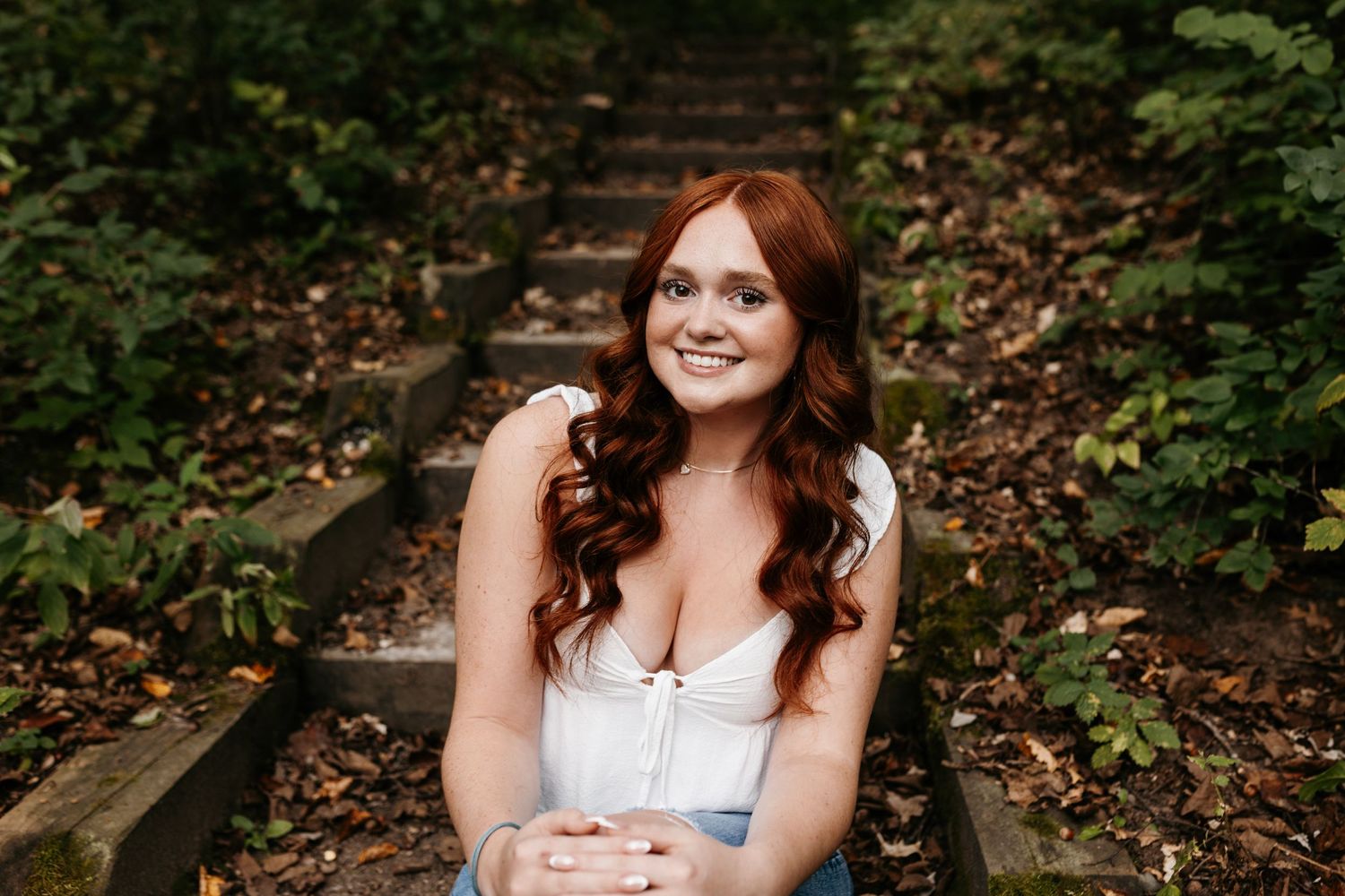 A portrait captures a woman in a white top sitting against a background of autumn leaves and stone steps.