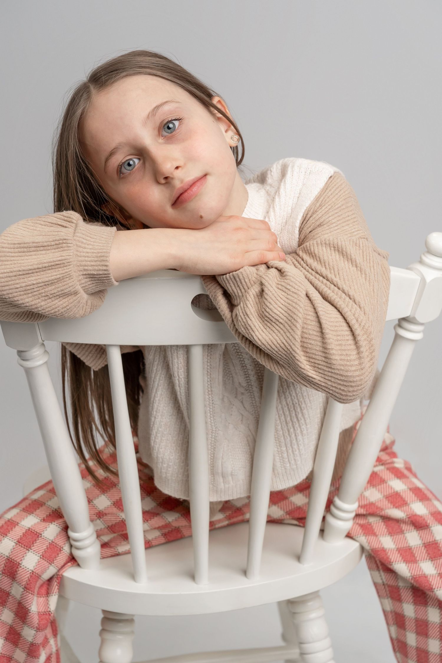Dreamy portrait on a white wooden chair with cozy sweater and checkered blanket.
