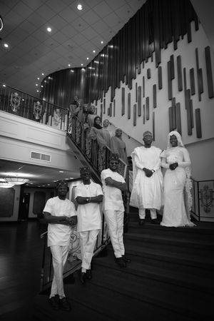 Black and white photo of elegantly dressed group posing on grand staircase in white traditional attire.