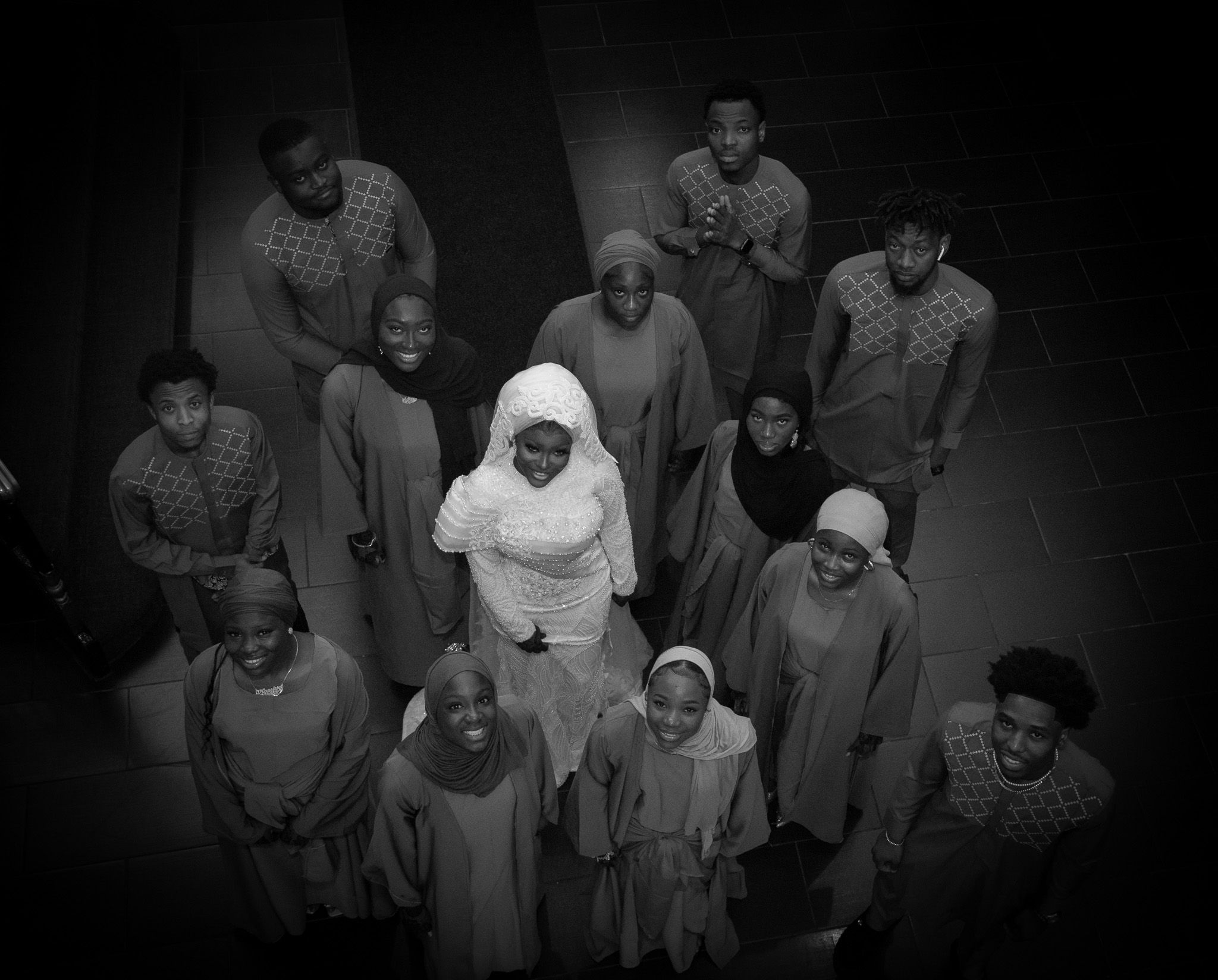 Black and white overhead photo of a diverse group of people in robes gathered together on a stage.