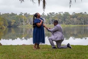A romantic proposal moment by a serene lake with Spanish moss draped trees in the background.