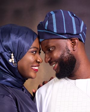 A couple in traditional African attire sharing an intimate moment while wearing navy blue and white garments.
