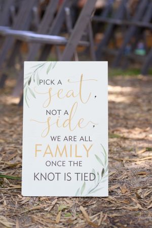 Wedding seating sign with gold lettering and greenery design on rustic ground.