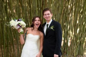 Happy newlyweds pose together against bamboo backdrop during wedding celebration.