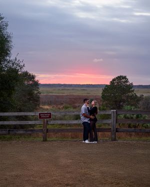 A couple sharing a romantic moment by a wooden fence during a vibrant pink sunset.