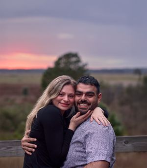 A joyful couple embracing while standing near a wooden fence at sunset.