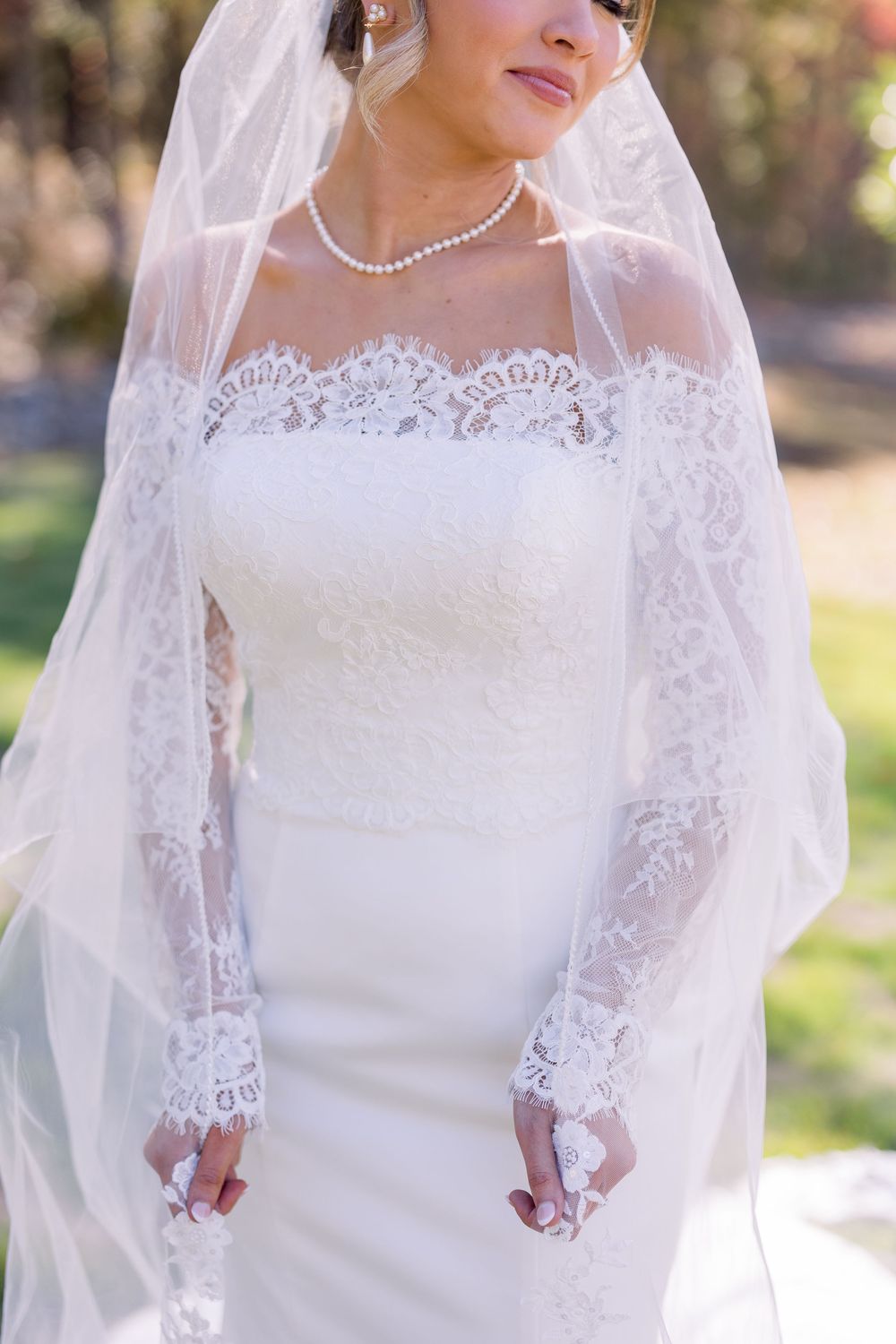 Close-up detail of a bride's lace wedding dress with pearl necklace and veil.