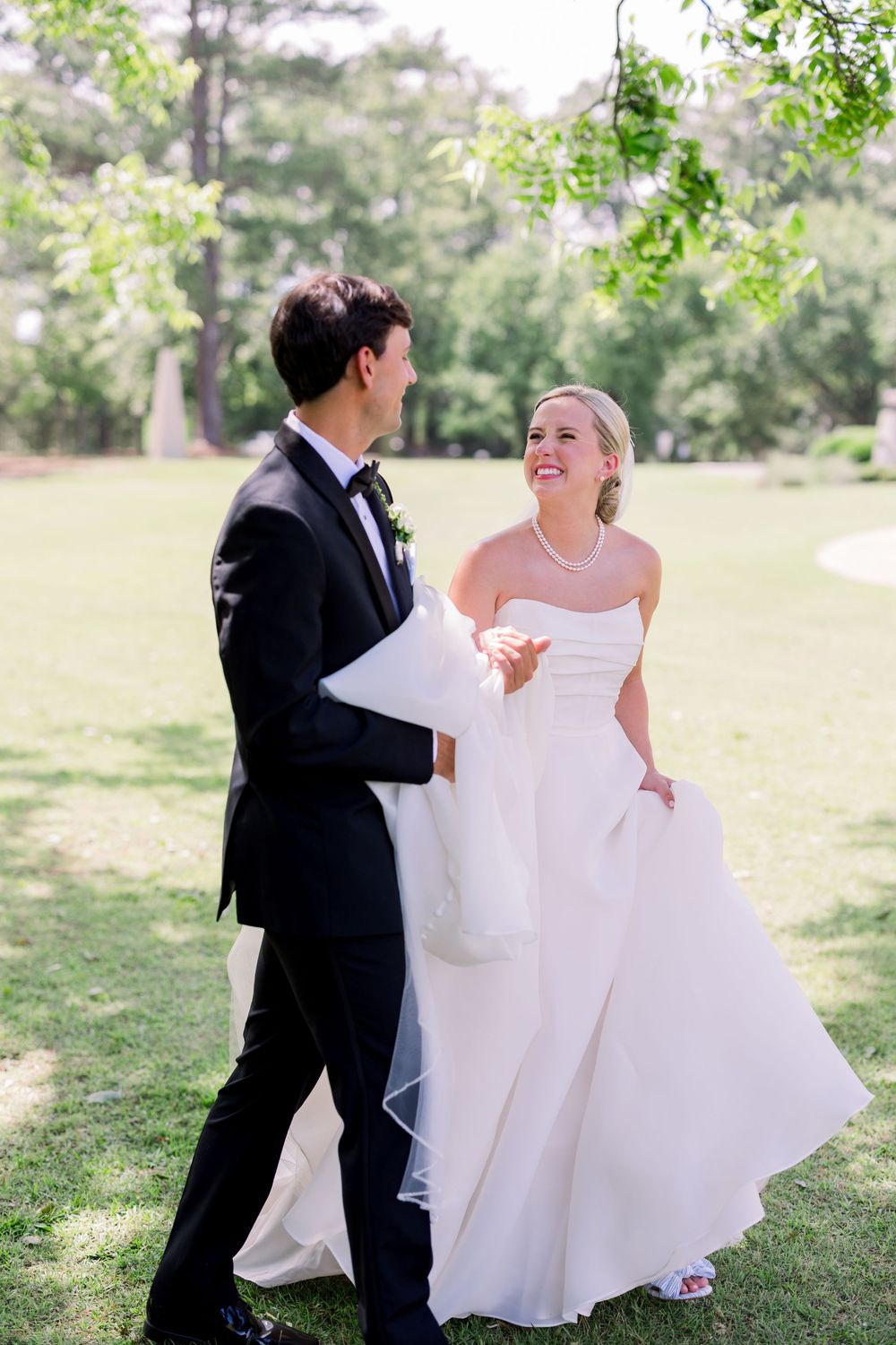 A couple playfully interacts in an outdoor setting, with the bride's white dress flowing in the breeze.