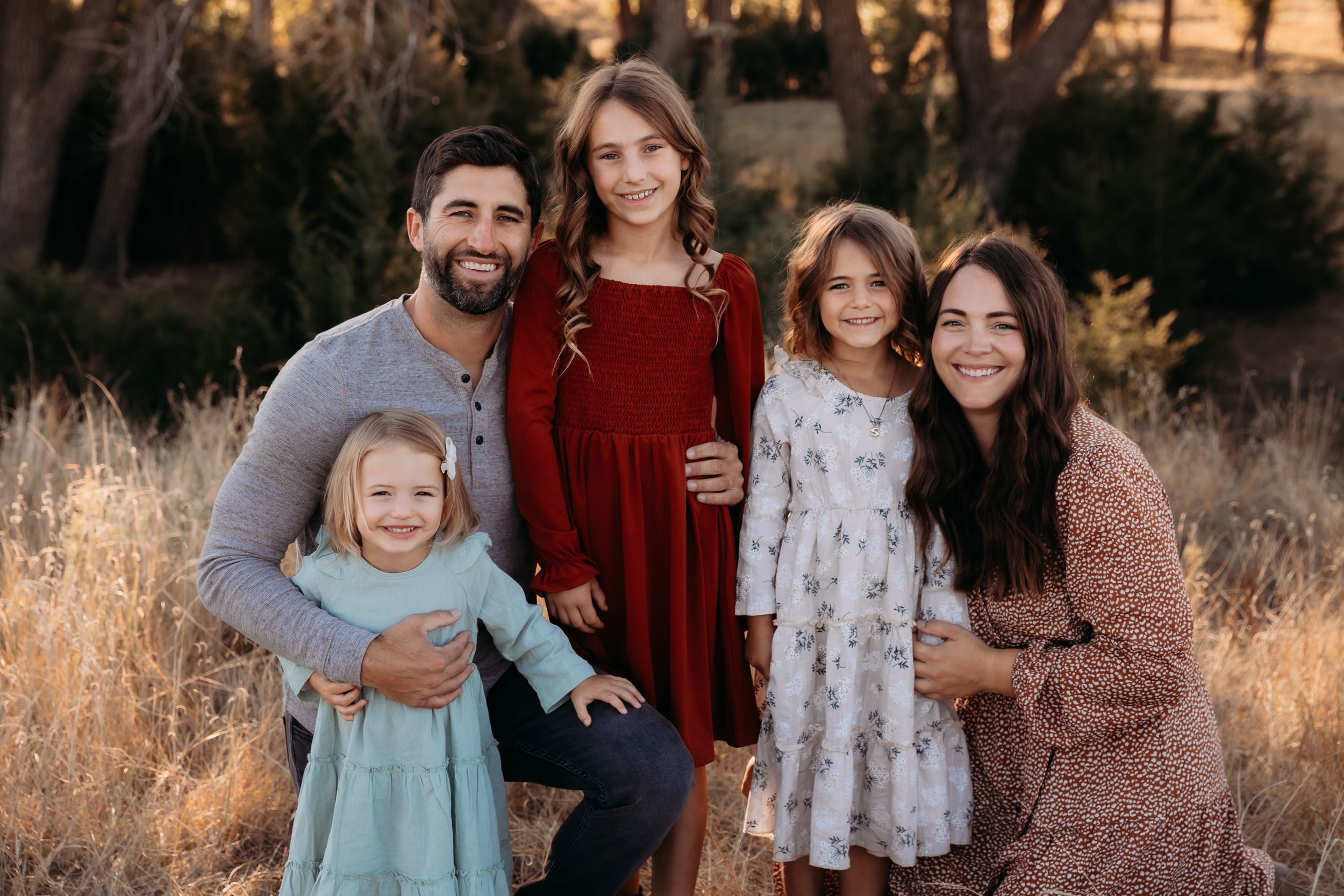 A family wearing coordinated burgundy and neutral tones poses together in a golden field at sunset.