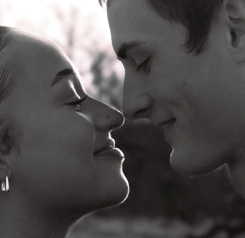Black and white photo of a young couple sharing a romantic moment, leaning in close for a kiss.