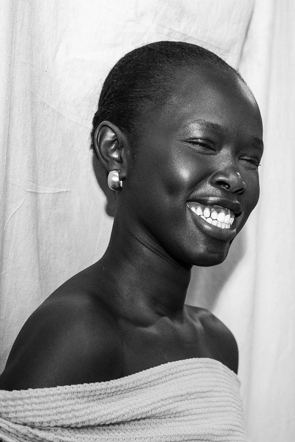 Black and white portrait of a joyful young woman with short hair, pearl earring, smiling broadly, bare shoulders.