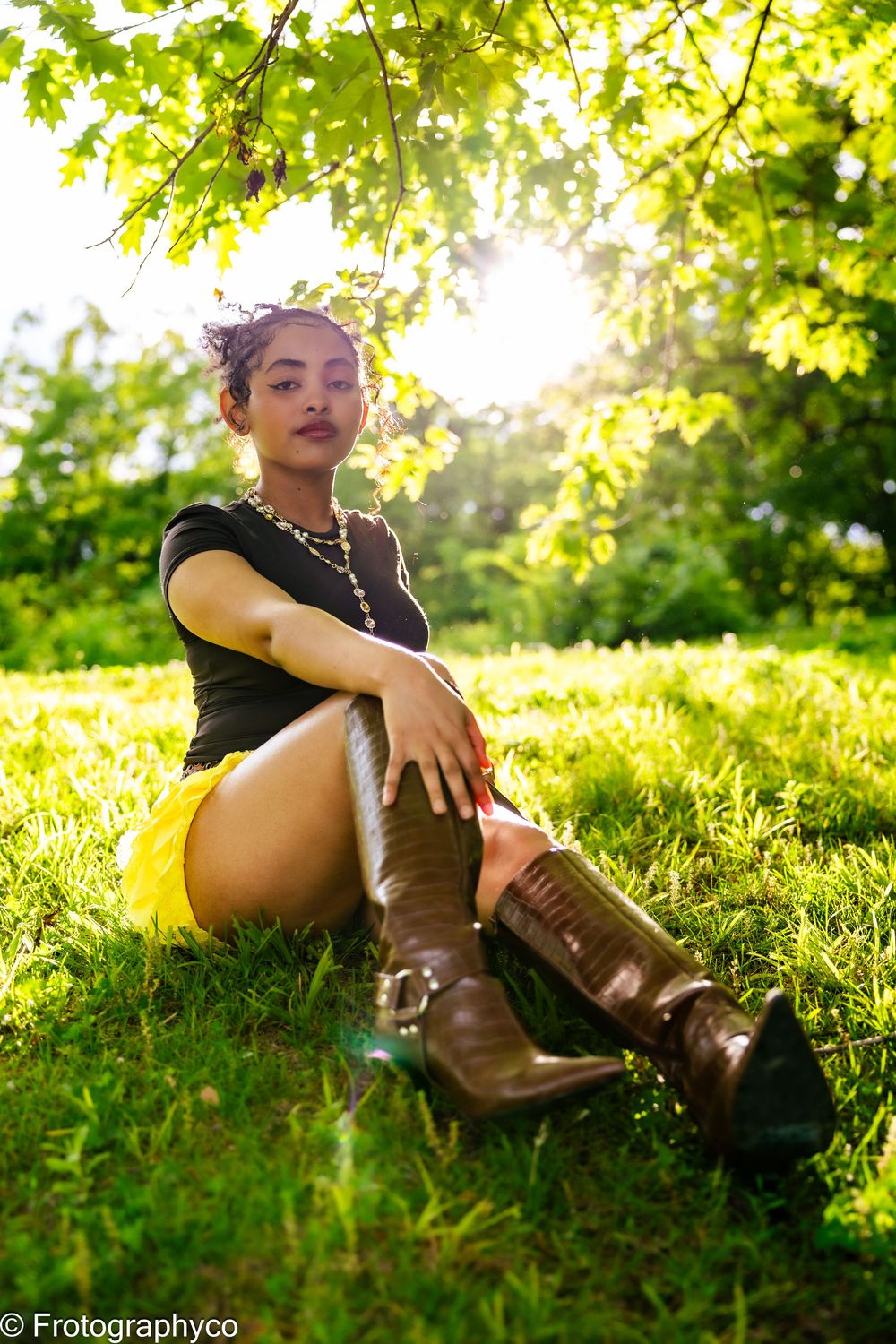Person relaxing in tall grass during golden hour sunlight wearing brown boots in a natural outdoor setting.
